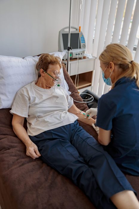 Doctor putting a drip in the arm of her patient in breathing mask during pandemic of Covid 19 Doctor putting drip in the arm of patient in mask during pandemic of Covid 19. High quality photo
